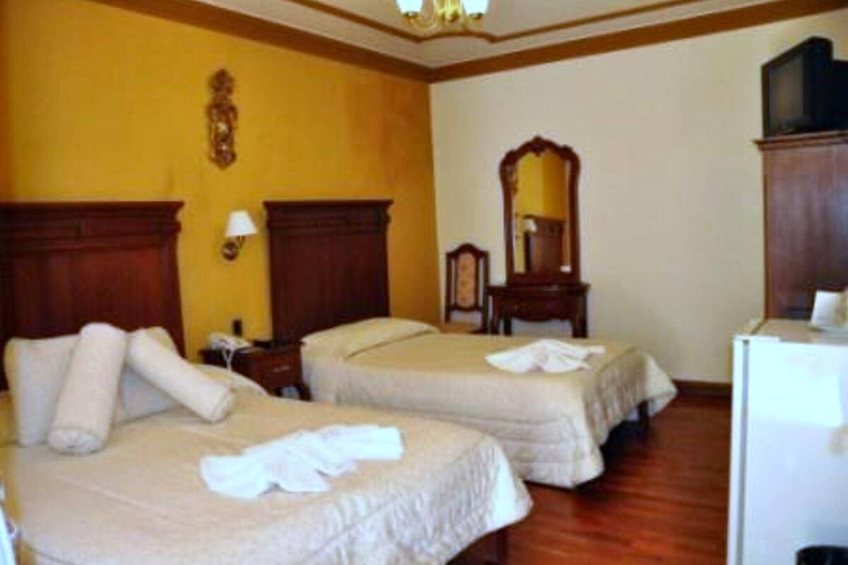 Habitación de hotel con dos camas, piso de madera, un espejo y un televisor.