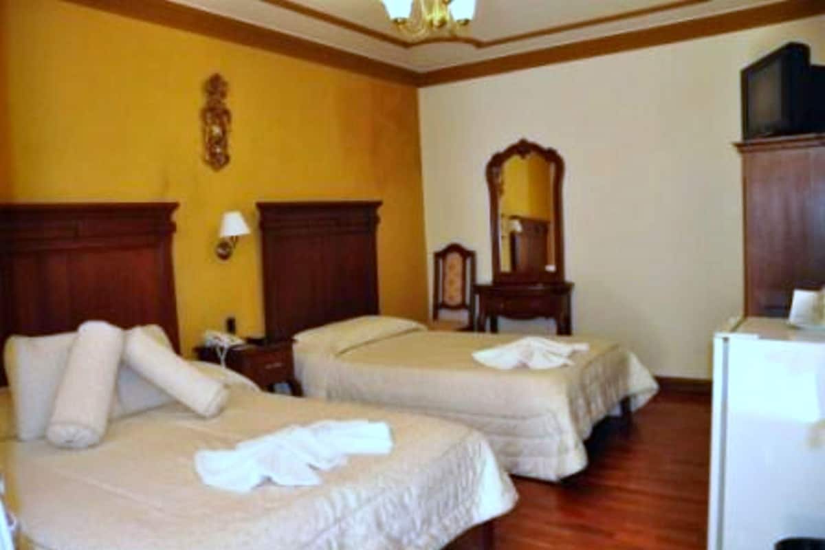 A hotel room with two beds, a wooden floor, a mirror, and a television.