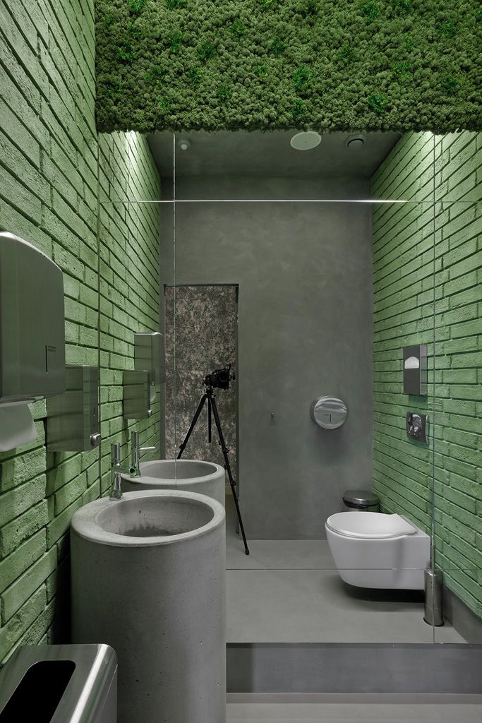 A modern bathroom with green brick walls, a large sink, a toilet, and a camera on a tripod.