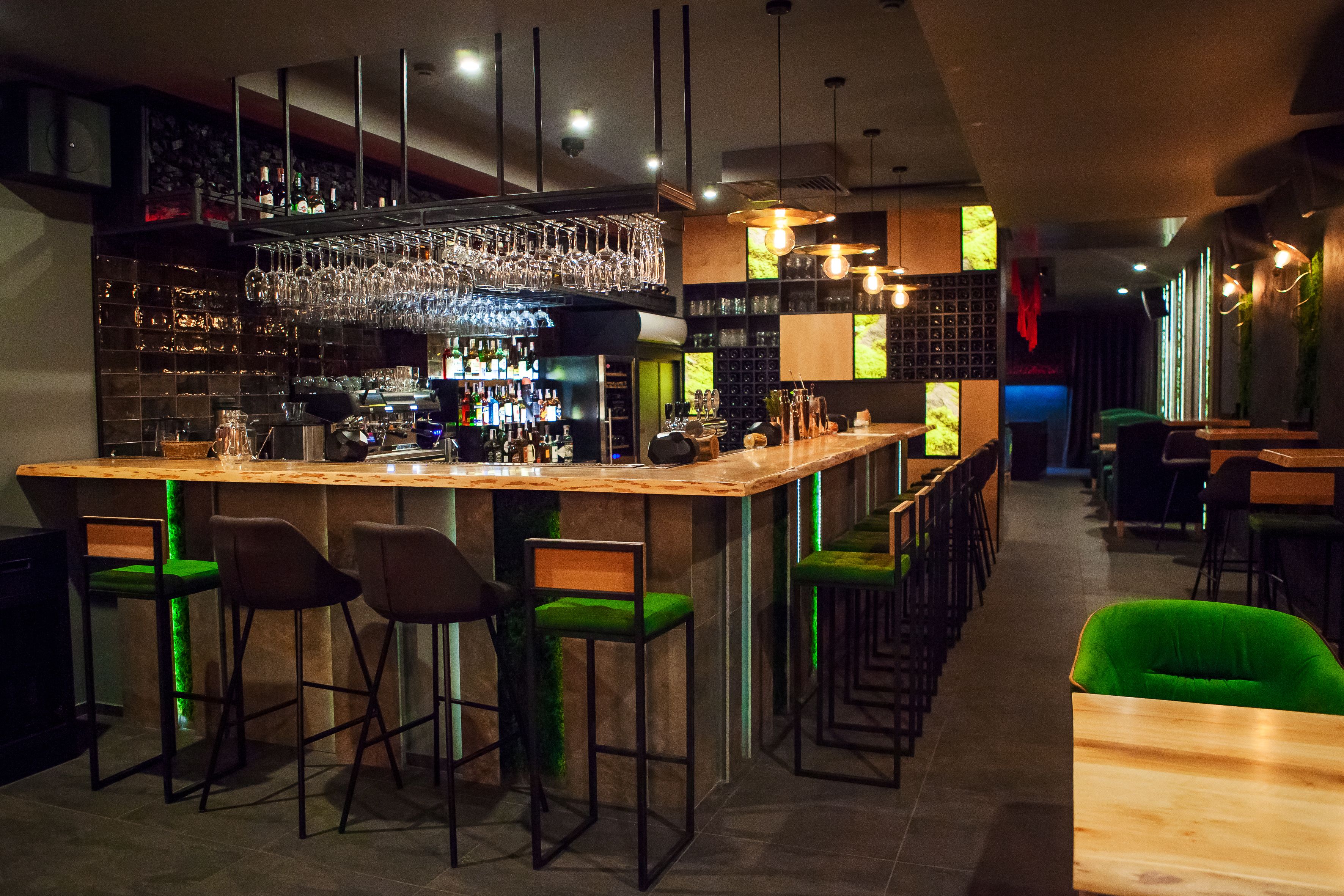 A bar area with a long counter, multiple stools, and a variety of bottles and glasses.