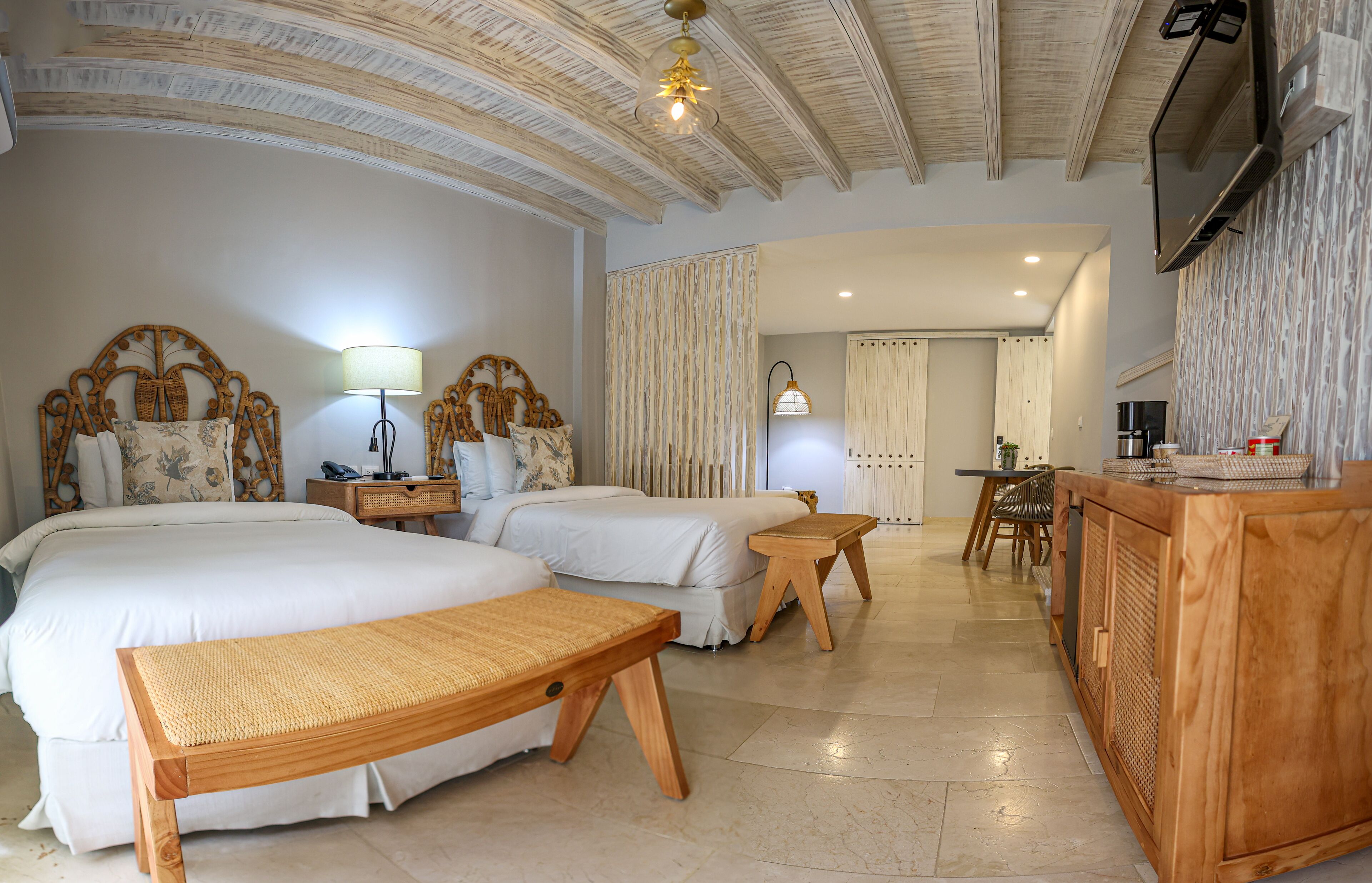 A hotel room with two beds, a wooden bench, a desk, and a TV mounted on the wall.