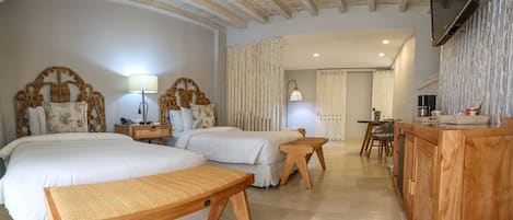 A hotel room with two beds, a wooden bench, a desk, and a TV mounted on the wall.