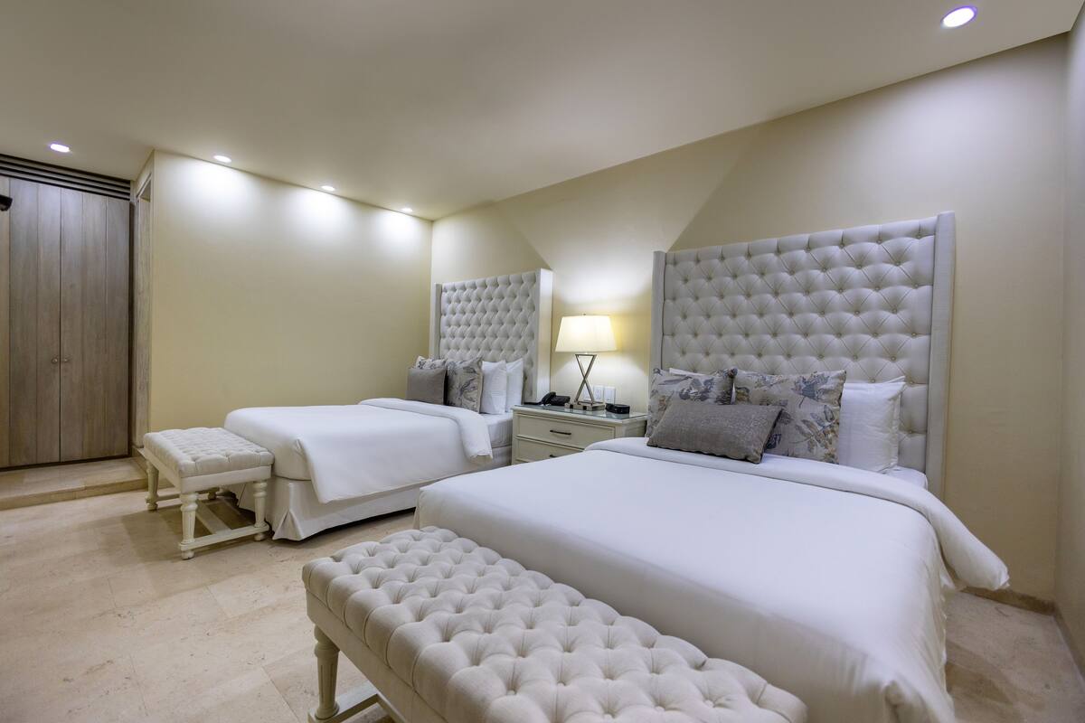 Une chambre avec deux lits, un banc et une table de chevet avec une lampe.