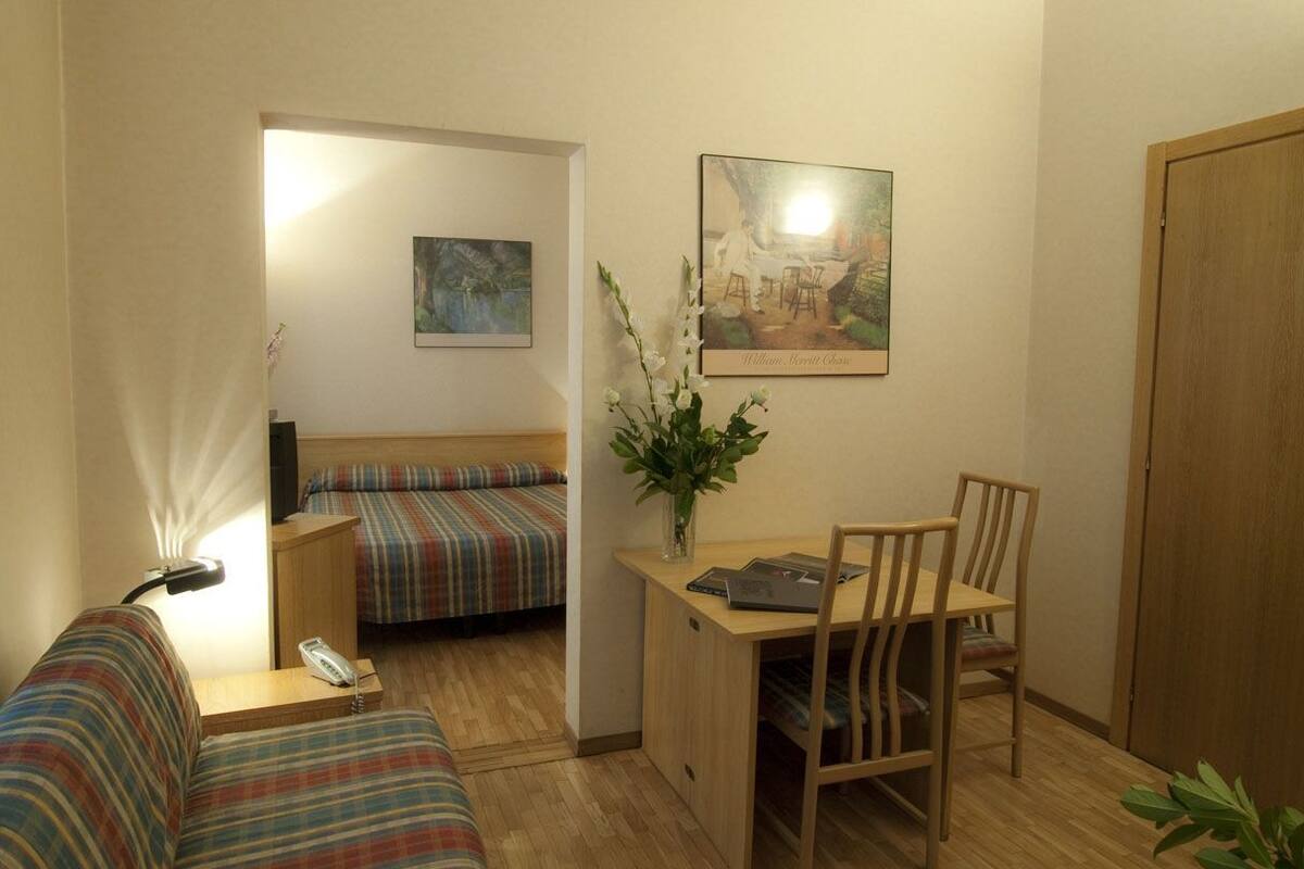 Una habitación pequeña y acogedora con una cama individual, un sofá, un escritorio con una silla y un armario de madera.