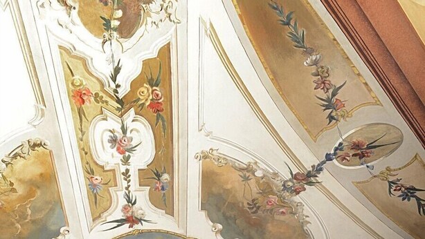 A ceiling with ornate floral and cherubic designs, a central circular medallion, and a wooden beam structure. - Residence Lagrange (Turin)