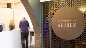 Un área de recepción con diseño moderno, incluyendo un letrero circular que dice "BEST WESTERN PLUS ALDHEM".