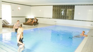 Una piscina interior con agua cristalina, una pared de azulejos con mosaicos y un área de descanso con tumbonas.