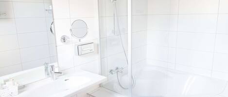 A modern bathroom with a white sink, mirror, and glass-enclosed shower.