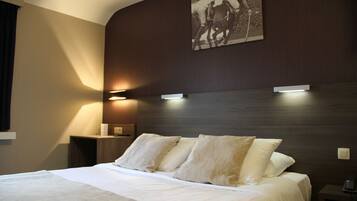 A neatly made bed with white linens and two pillows, a bedside table with a lamp, and a wall-mounted artwork depicting a horse race.