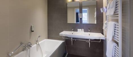 Un baño moderno con bañera, dos lavamanos y un espejo grande.