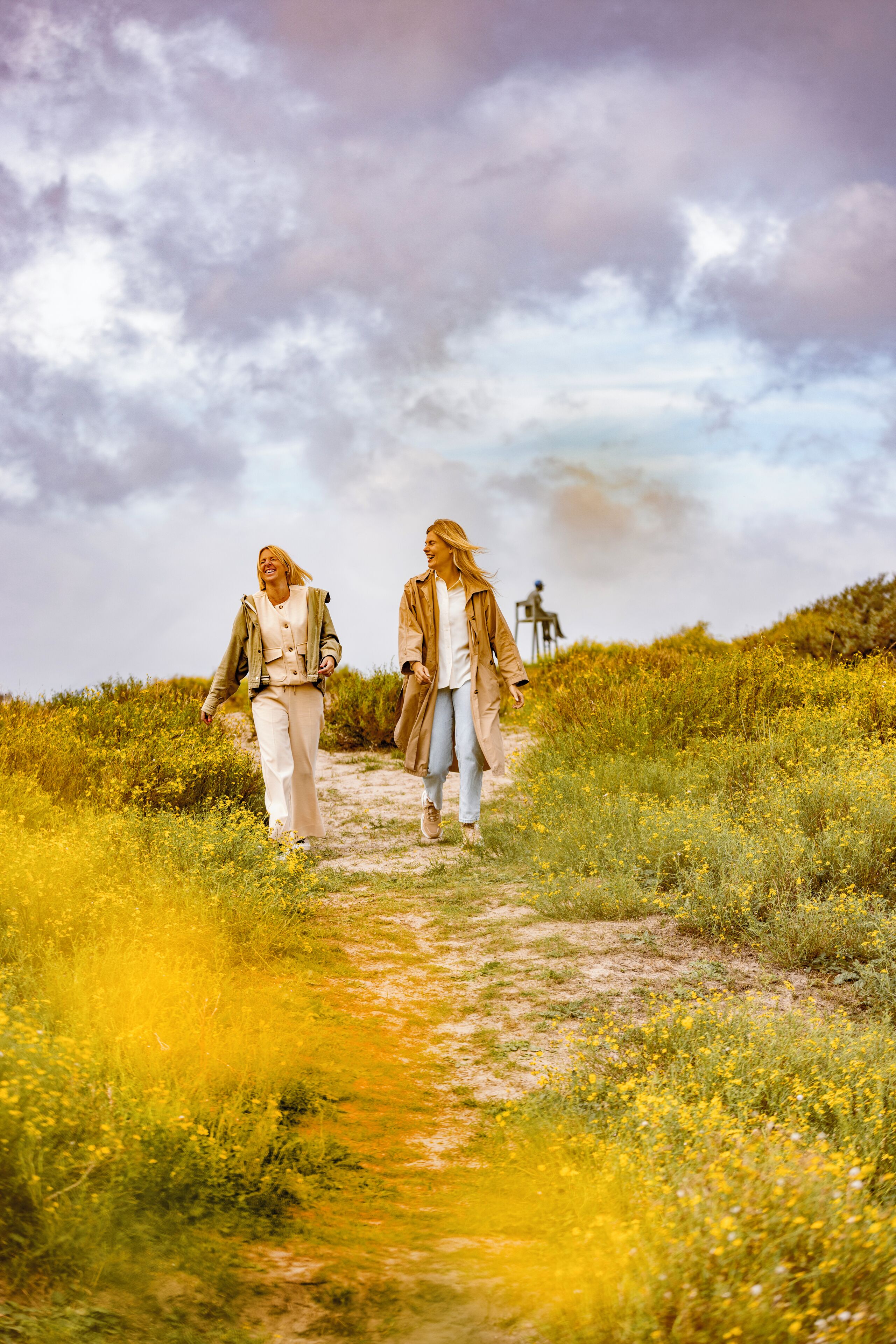 Dos personas caminando por un sendero de tierra rodeado de flores amarillas.
