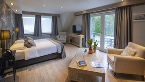 A modern hotel room with a large bed, a sofa, a coffee table, a desk with a TV, and a balcony with a view. - Auberge St. Pol (Knokke-Heist)