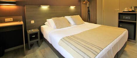 Una habitación de hotel con una cama grande, mesitas de noche, un armario y un escritorio.