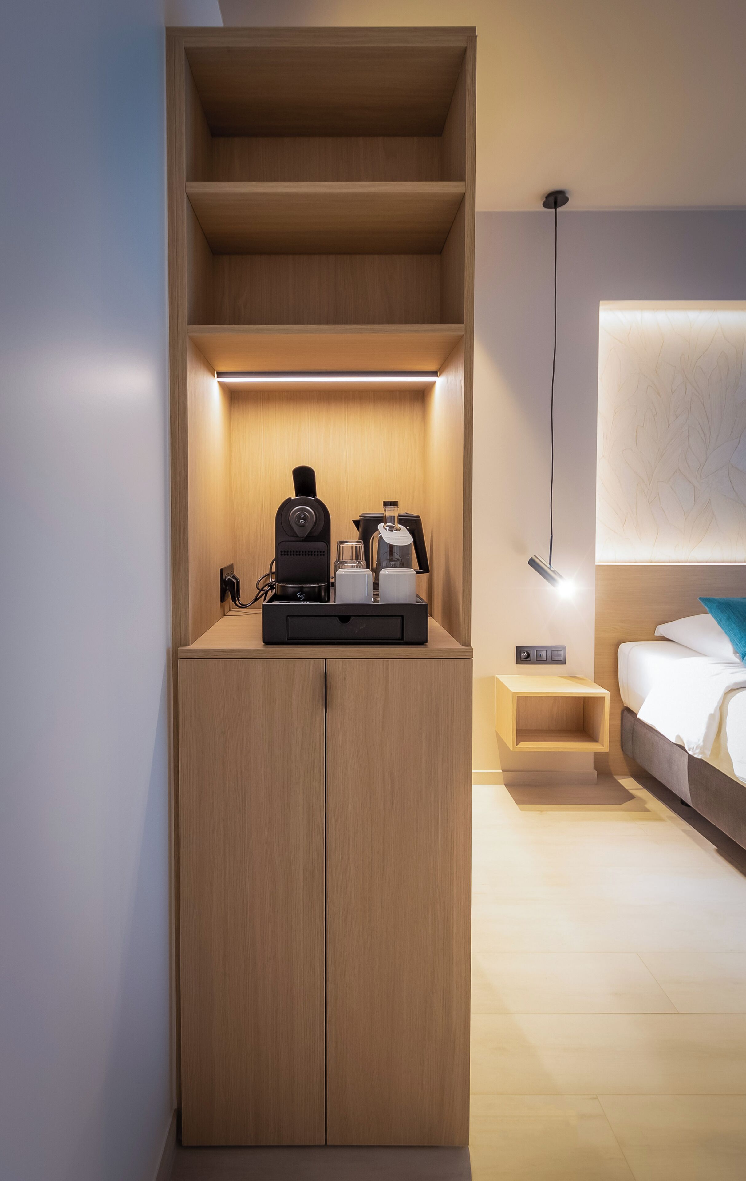 A modern bedroom with a wooden wardrobe, a bedside table with a lamp, and a bed with a blue pillow.