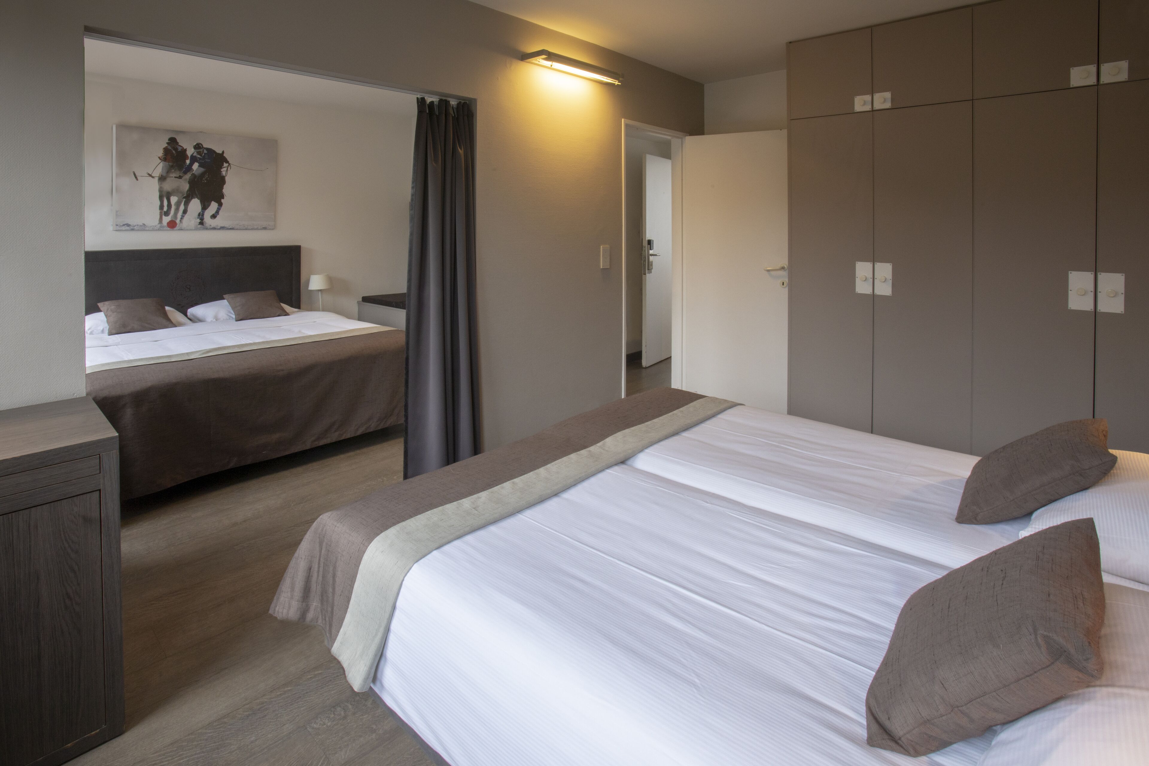 Habitación de hotel con dos camas, un armario, una mesita de noche y un cuadro en la pared.