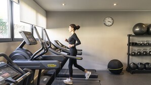 Uma academia com esteiras, um relógio de parede e uma estante com bolas de exercício e halteres.