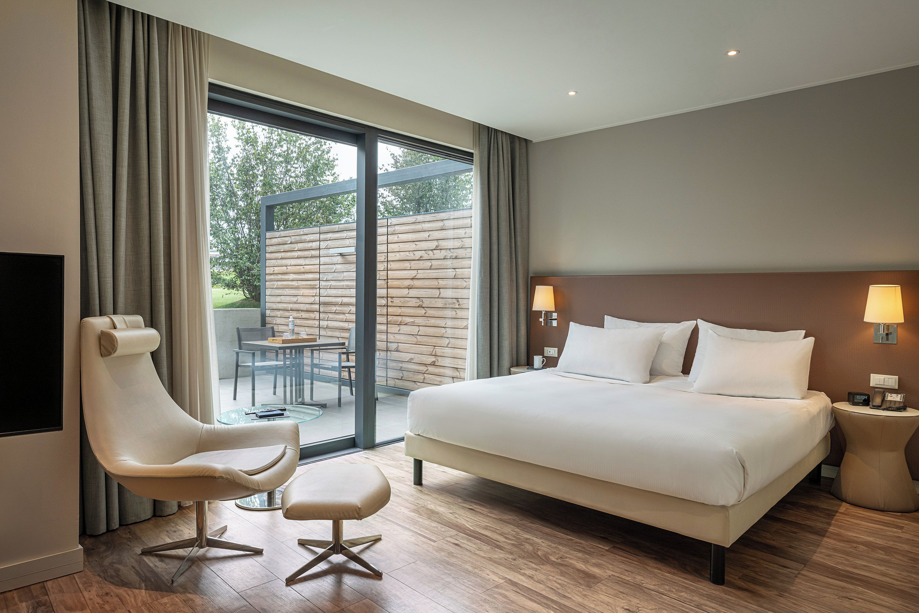 Habitación de hotel con una cama grande, zona de estar con una silla y mesa, televisión y vistas al exterior.