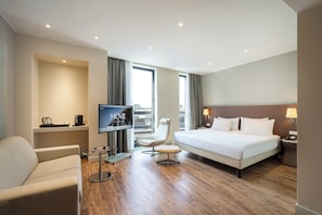 Habitación de hotel con cama, una silla, escritorio con computadora, televisor y ventana con cortinas.