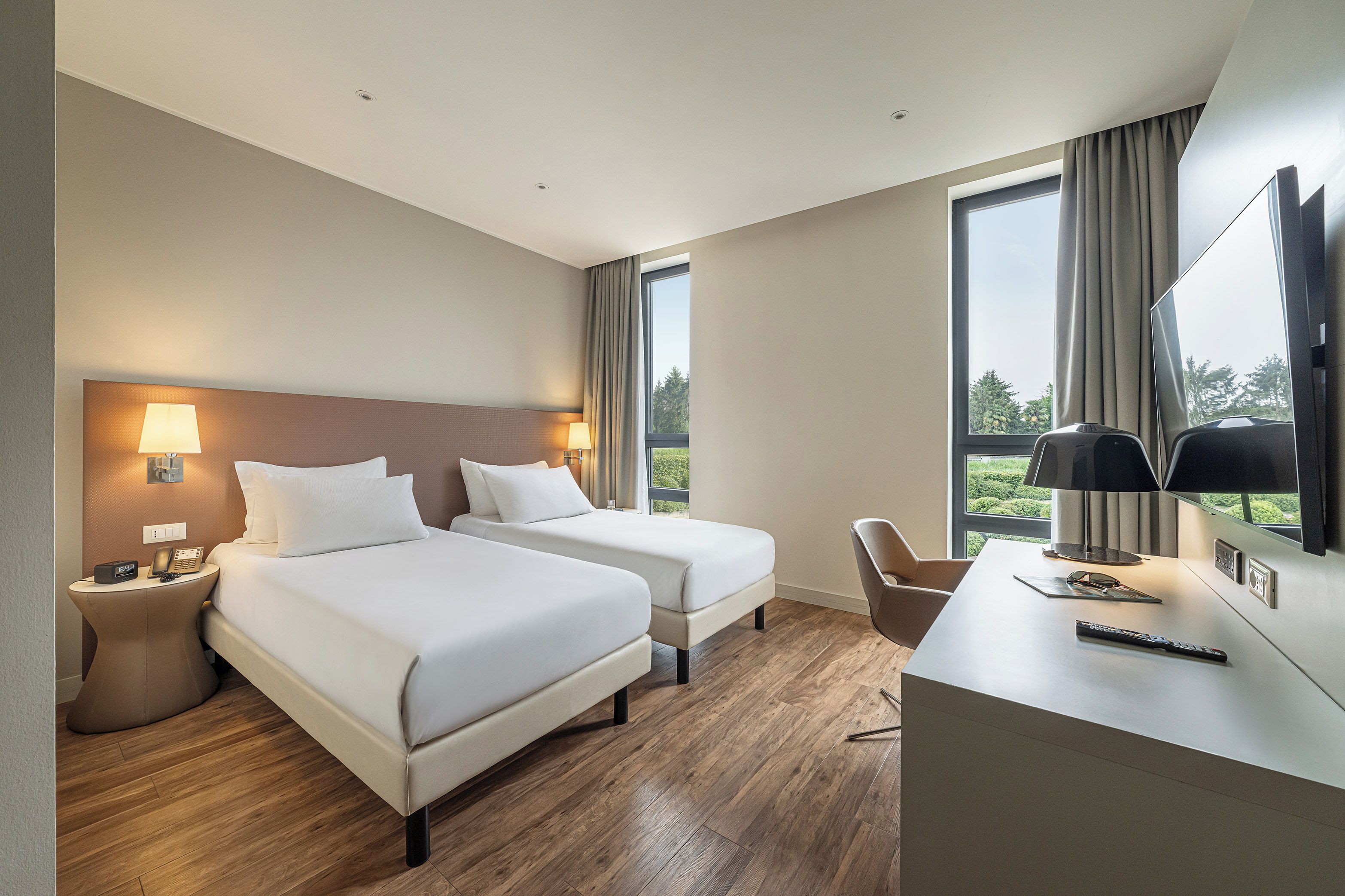 Habitación de hotel con dos camas, un escritorio, una silla, un televisor y una ventana con cortinas.