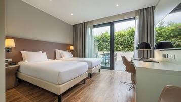 Habitación de hotel con dos camas, un escritorio y vistas a zonas verdes.