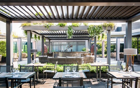 An outdoor patio area with tables and chairs, a bar, and greenery.