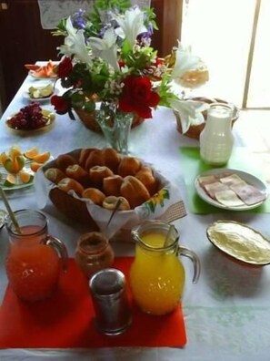 Una mesa de desayuno con diversas comidas, un florero de flores y una jarra de jugo de naranja.