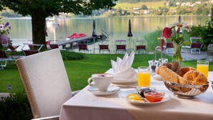 A table set for breakfast with a view of a lake, including a bowl of bread, a cup of coffee, and a glass of orange juice. - Seewinkel (Fuschl am See)