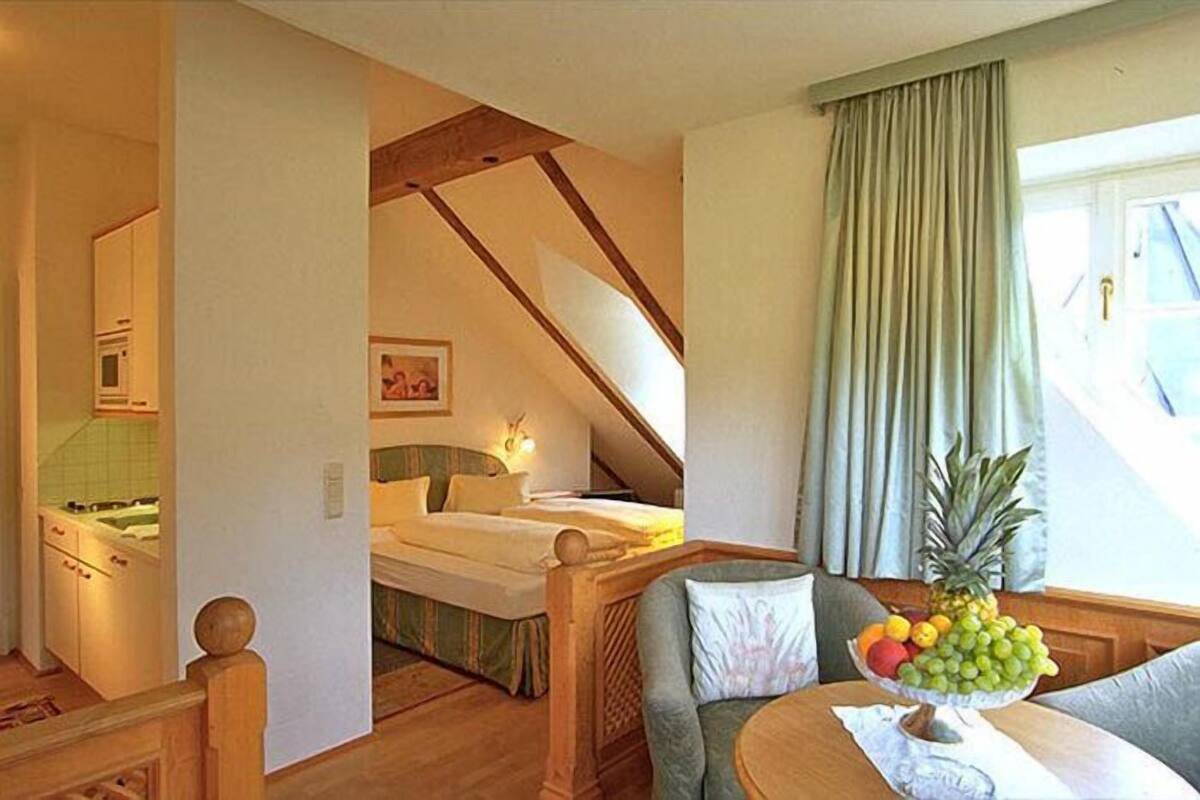 A cozy room with a bed, a dining table with fruit, and a kitchen area.
