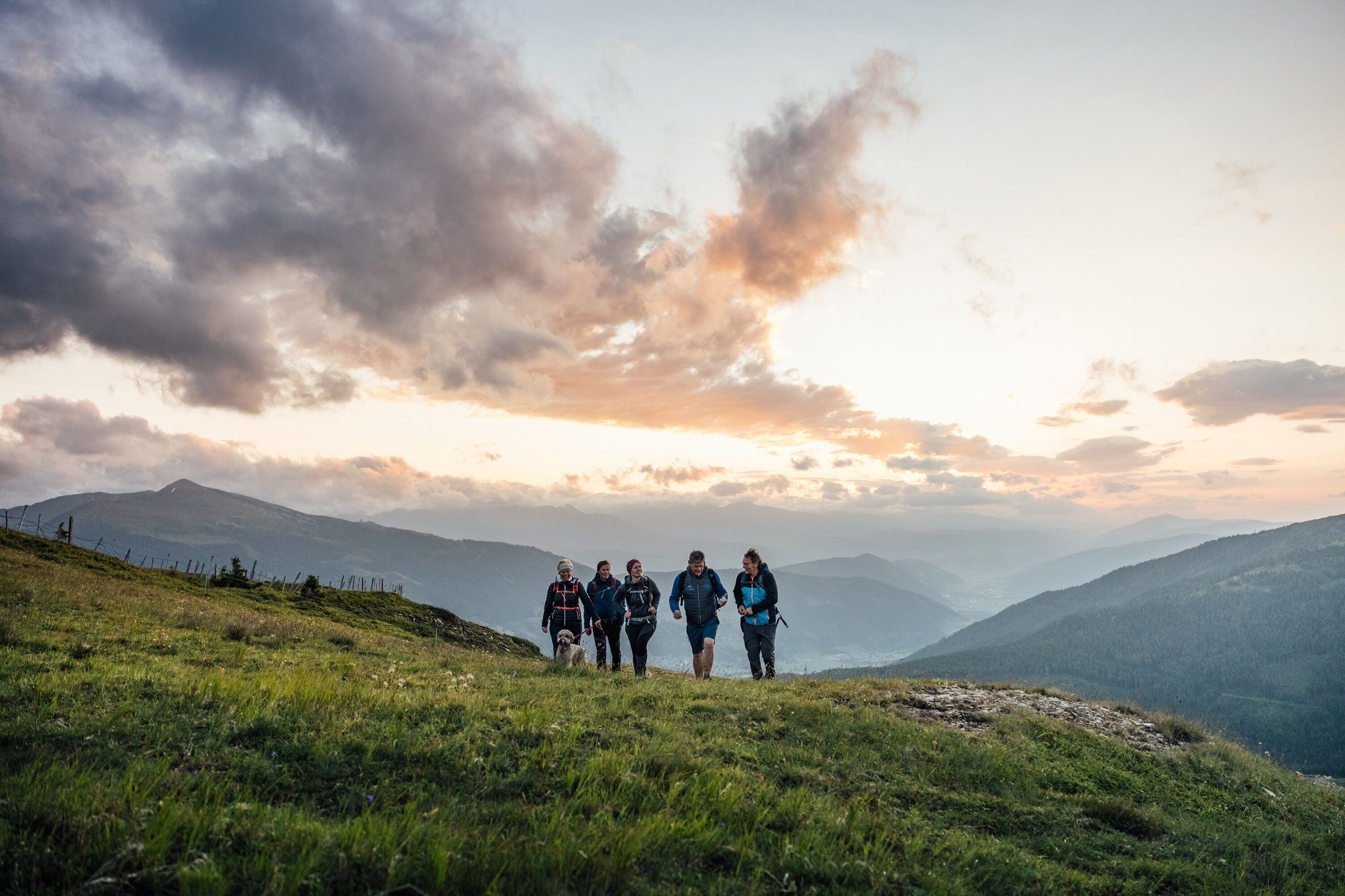 Un groupe de personnes se promène sur une colline verdoyante, avec un paysage montagneux en arrière-plan.