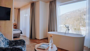 Un dormitorio moderno con un ventanal grande, una bañera, una cama y un televisor.