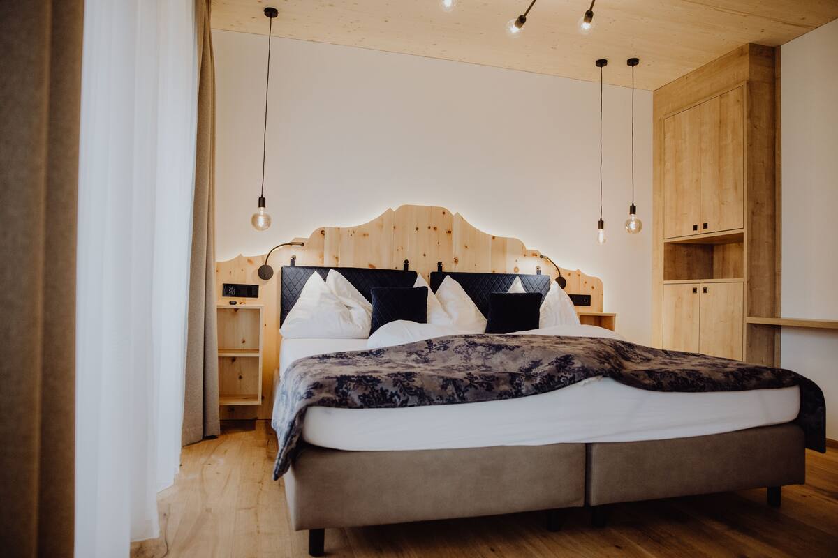A bedroom with a wooden headboard, a bed with white and dark bedding, and a wooden wardrobe.