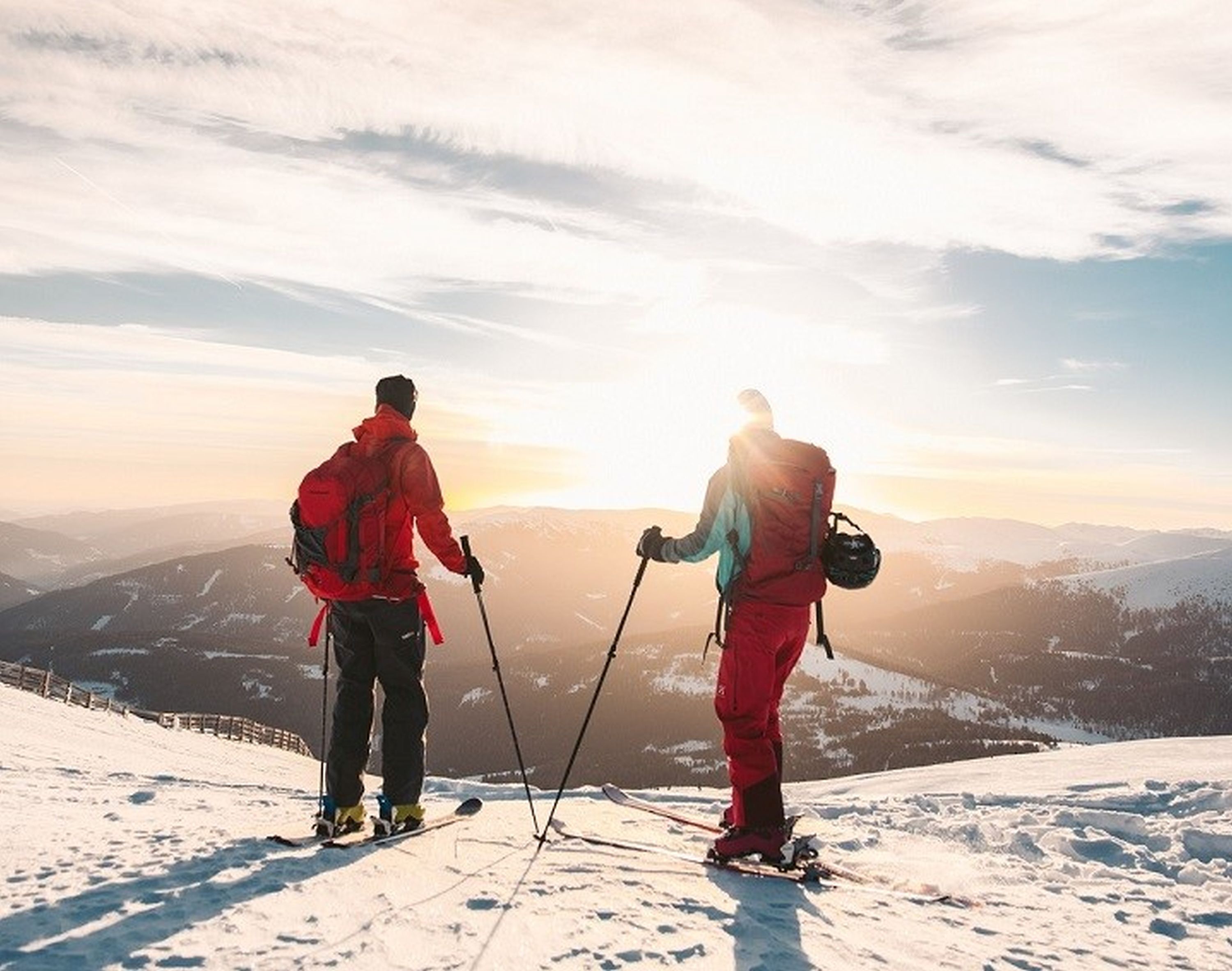 Dos personas esquiando en una montaña nevada, con un atardecer de fondo.