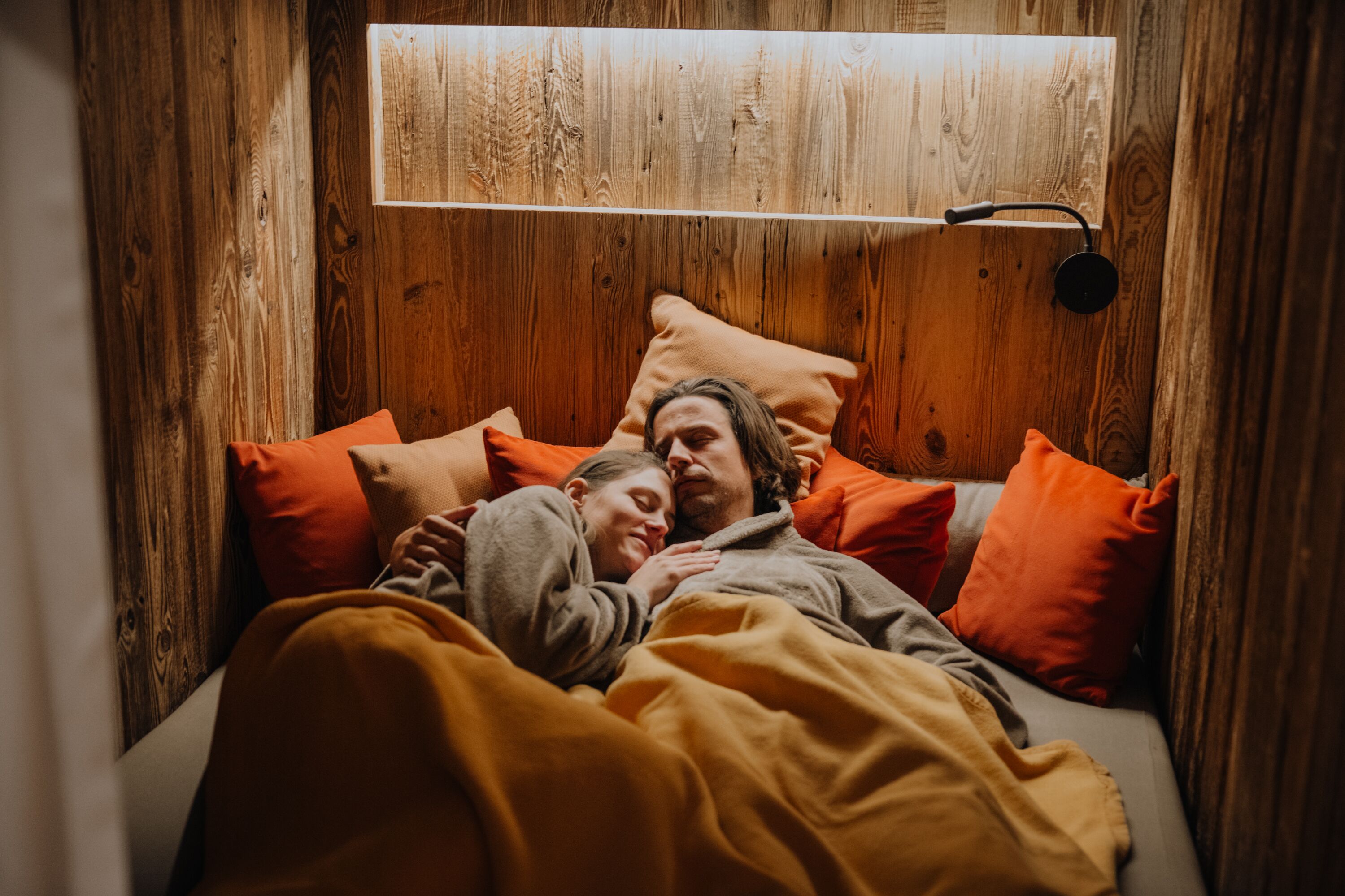 Een gezellige houten kamer met een bed, kussens en een wandlamp.