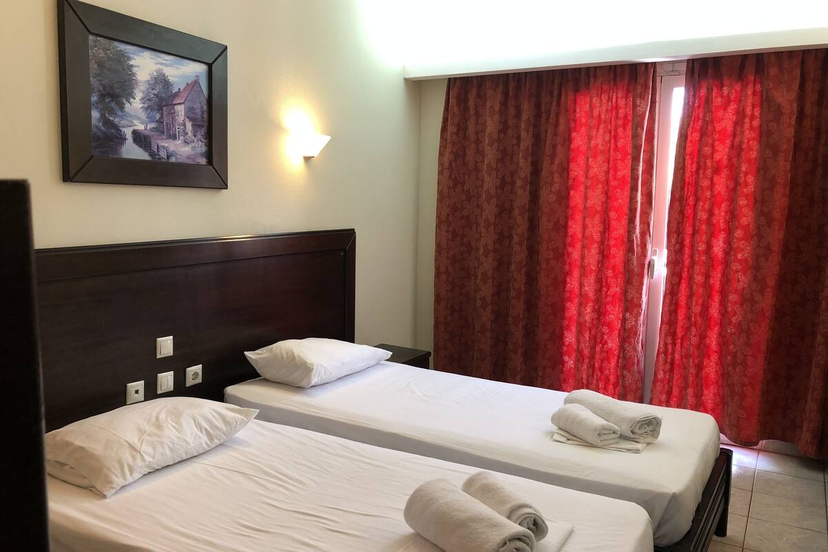 Habitación de hotel con dos camas, un cuadro en la pared, una luz de noche y cortinas rojas.