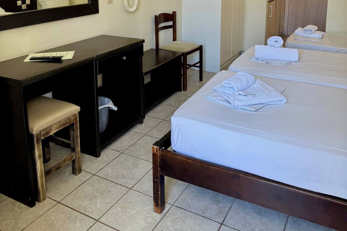 Ein Hotelzimmer mit einem Bett, einem Schreibtisch, einem Stuhl, einem Spiegel, einem Fernseher und einem an der Wand montierten Telefon.