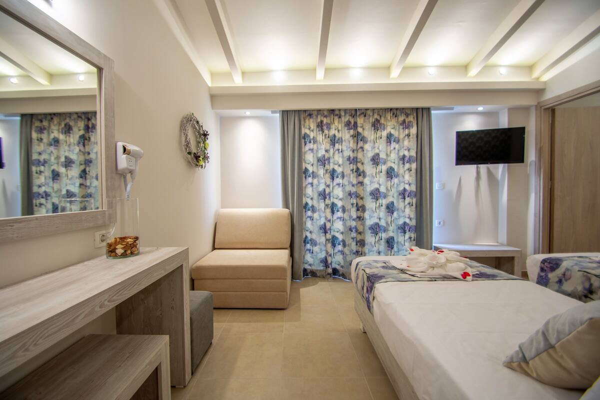 Ein Hotelzimmer mit einem Bett, einer Couch, einem Fernseher, einem Spiegel und einem Fön an der Wand.