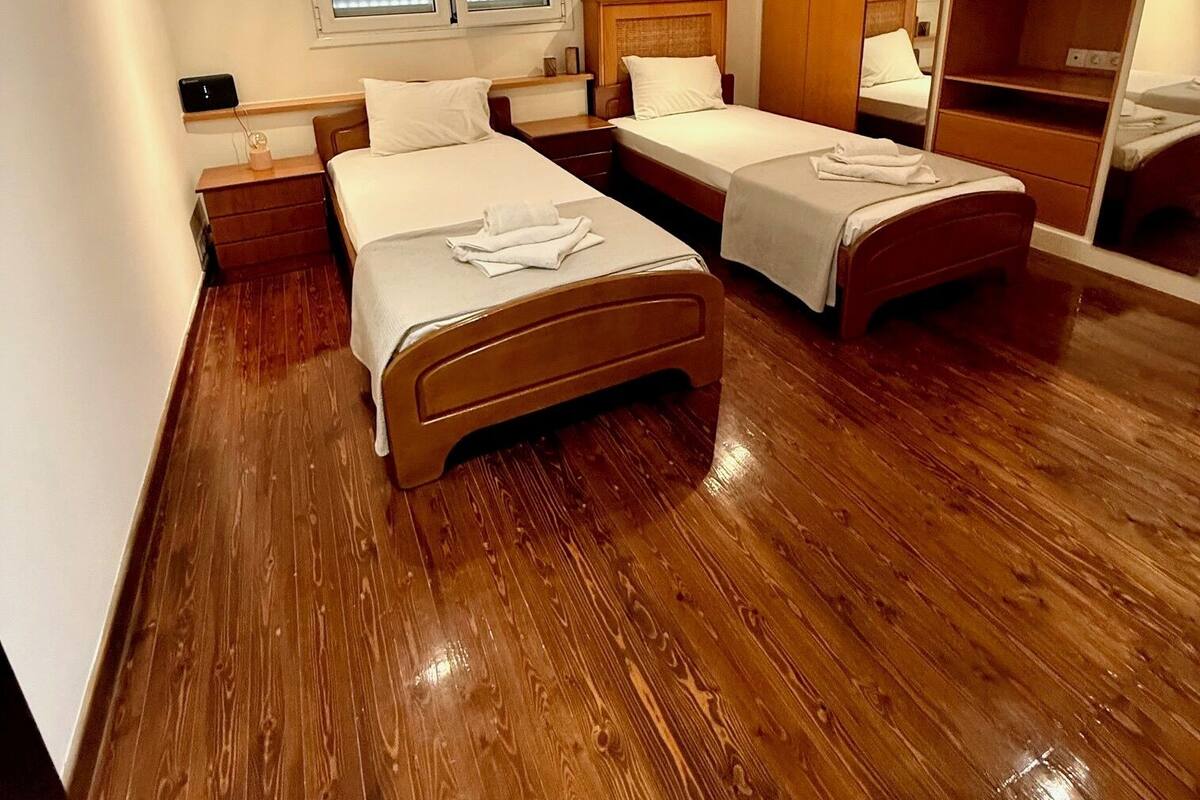 Habitación de hotel con dos camas, suelo de madera, un espejo grande y una ventana con persianas.