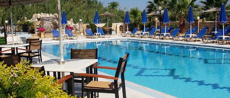 A poolside area with lounge chairs, umbrellas, and a clear blue pool.