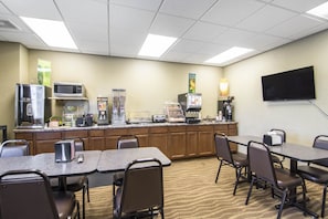 A hotel room with a kitchenette, a flat-screen TV, and a dining area with tables and chairs.