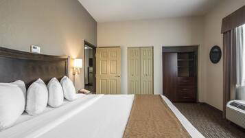 Quarto de hotel com uma cama grande, abajur, guarda-roupa e espelho na parede.