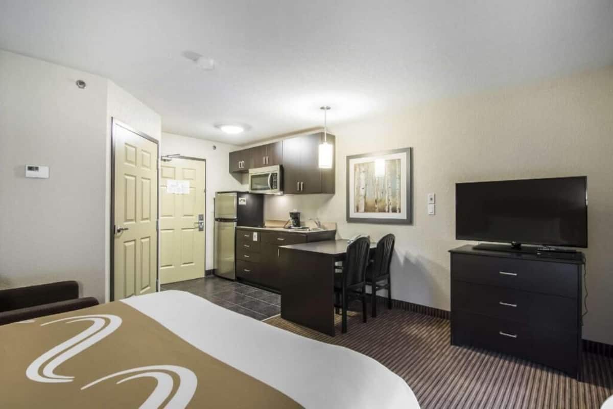 A hotel room with a bed, a desk with a chair, a television, a microwave, and a small kitchenette.