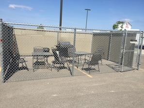 A fenced outdoor area with a table and chairs, a grill, and a trash can.
