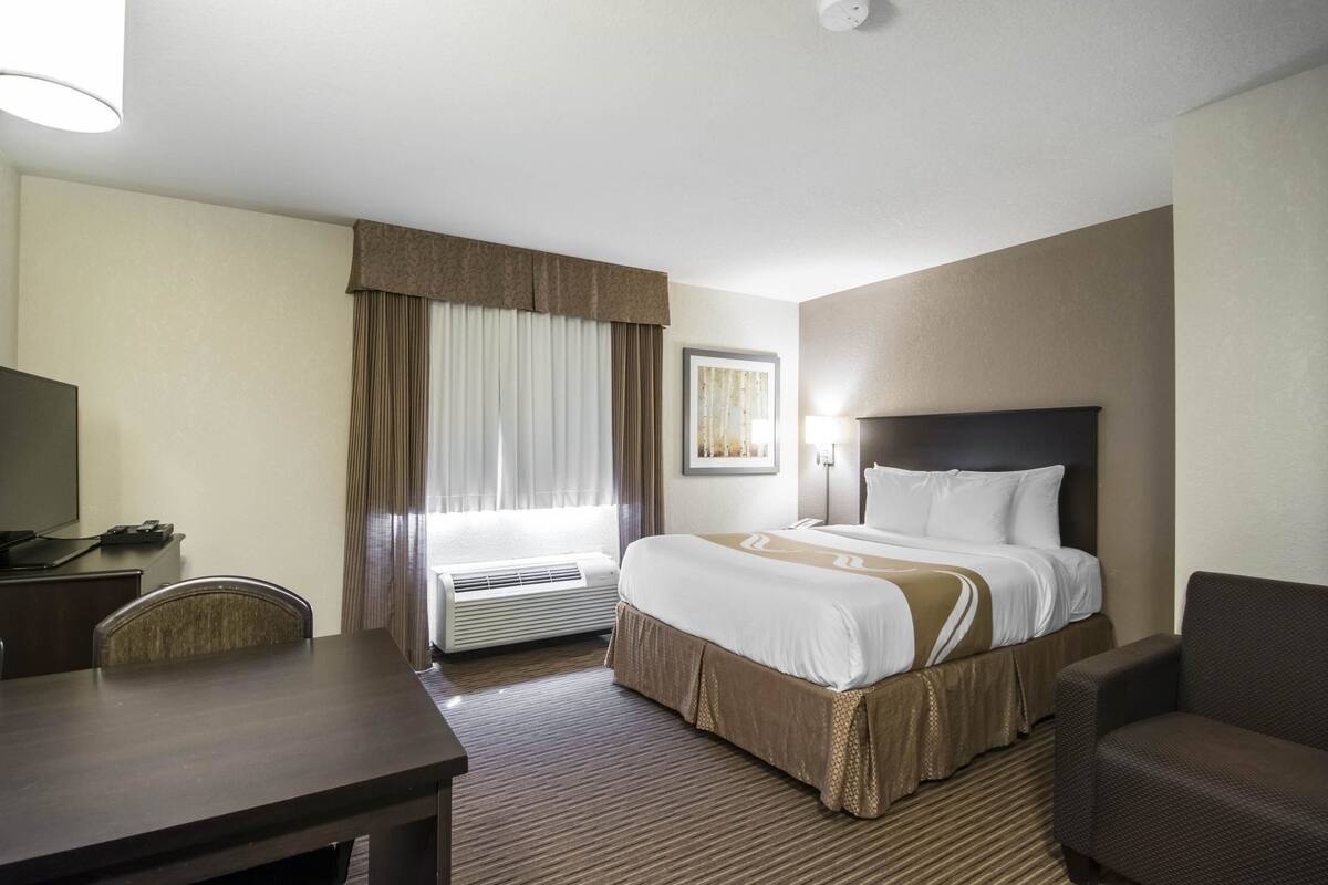 A hotel room with a bed, a desk, a chair, and a window with curtains.