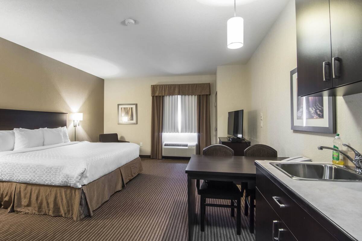 A hotel room with a bed, a desk with a chair, a sink, and a television.