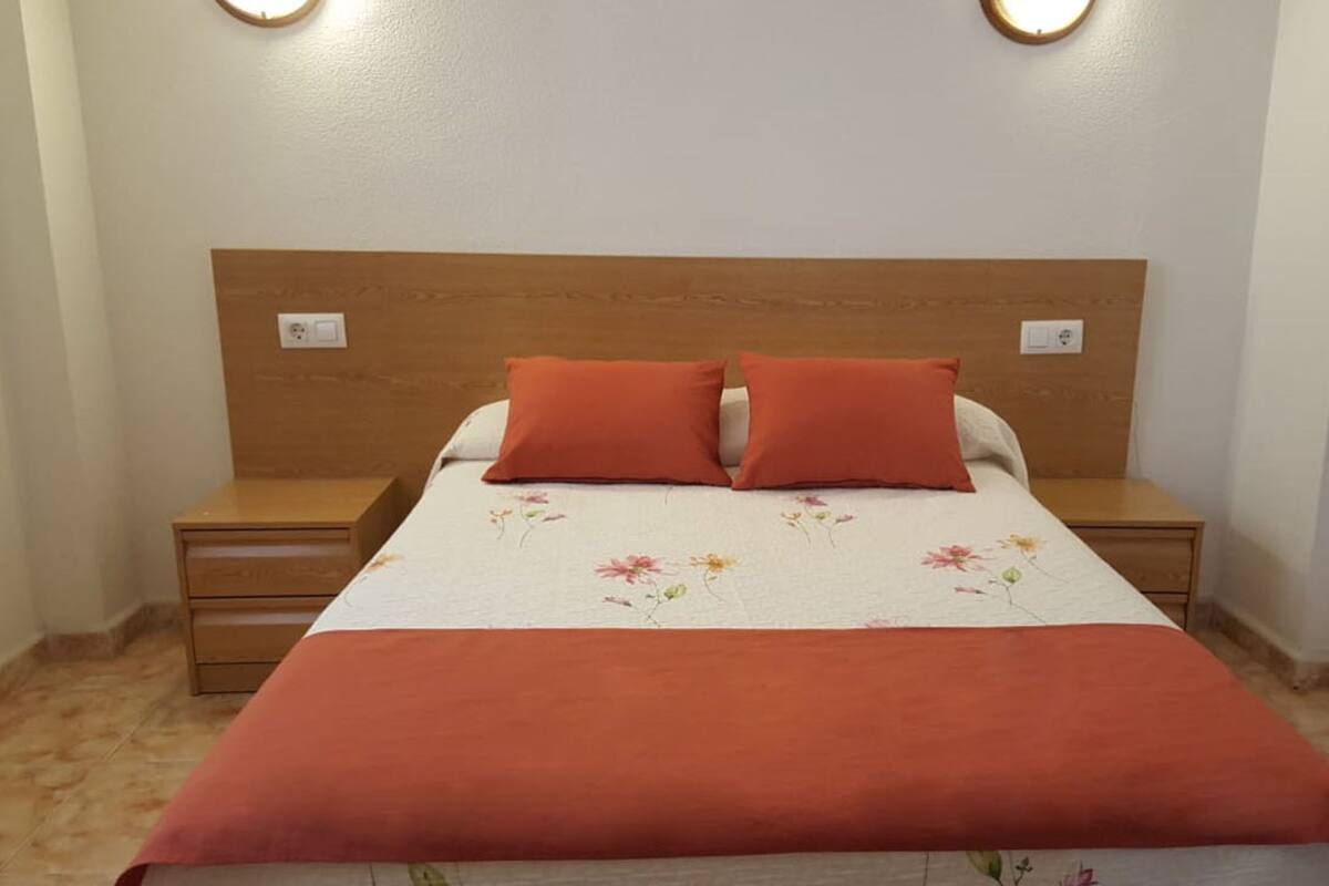 A bedroom with a wooden headboard, two matching pillows, a floral bedspread, and two bedside tables with lamps.