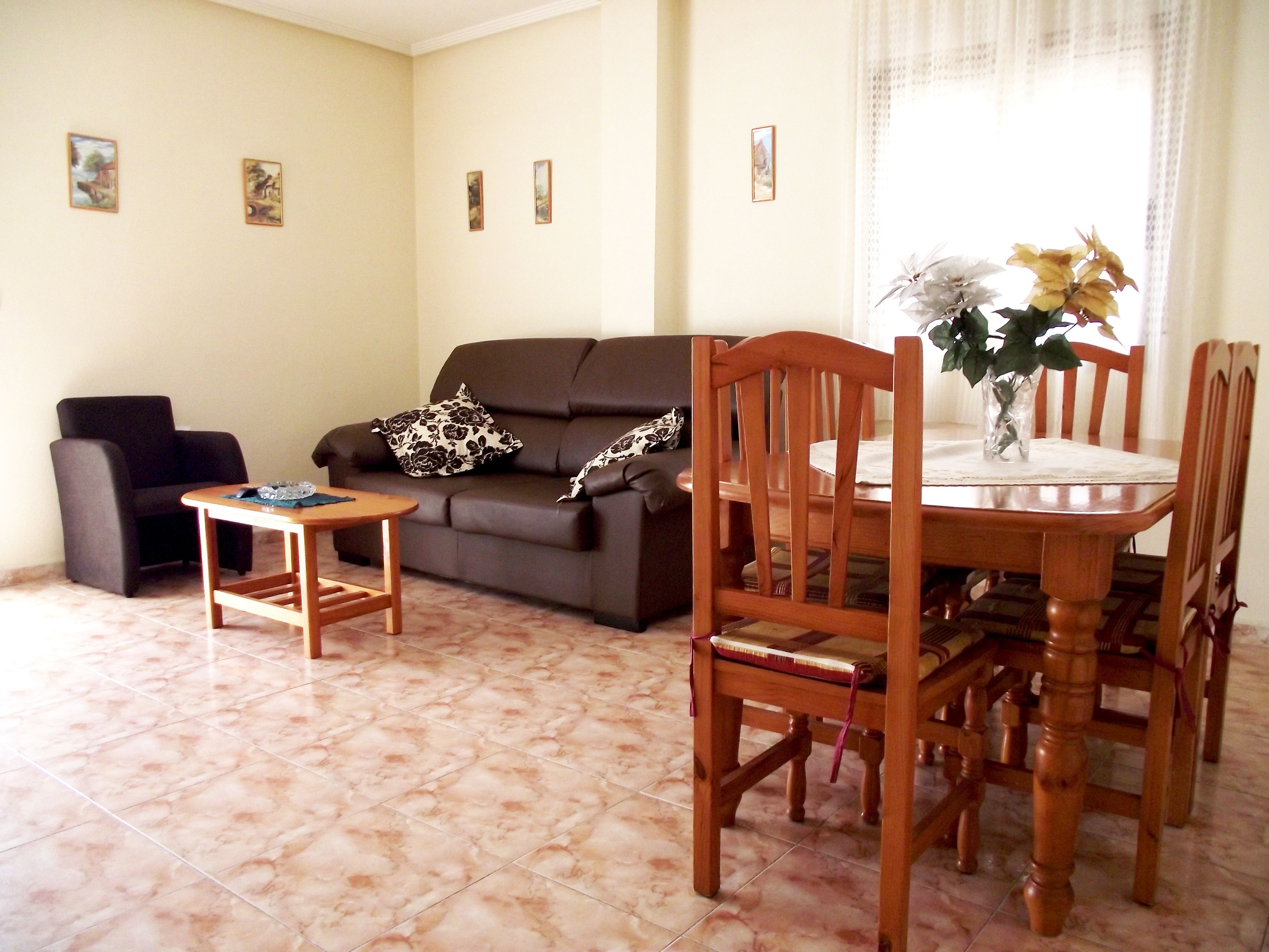 A living room with a sofa, a coffee table, a dining table with chairs, and a vase with flowers.