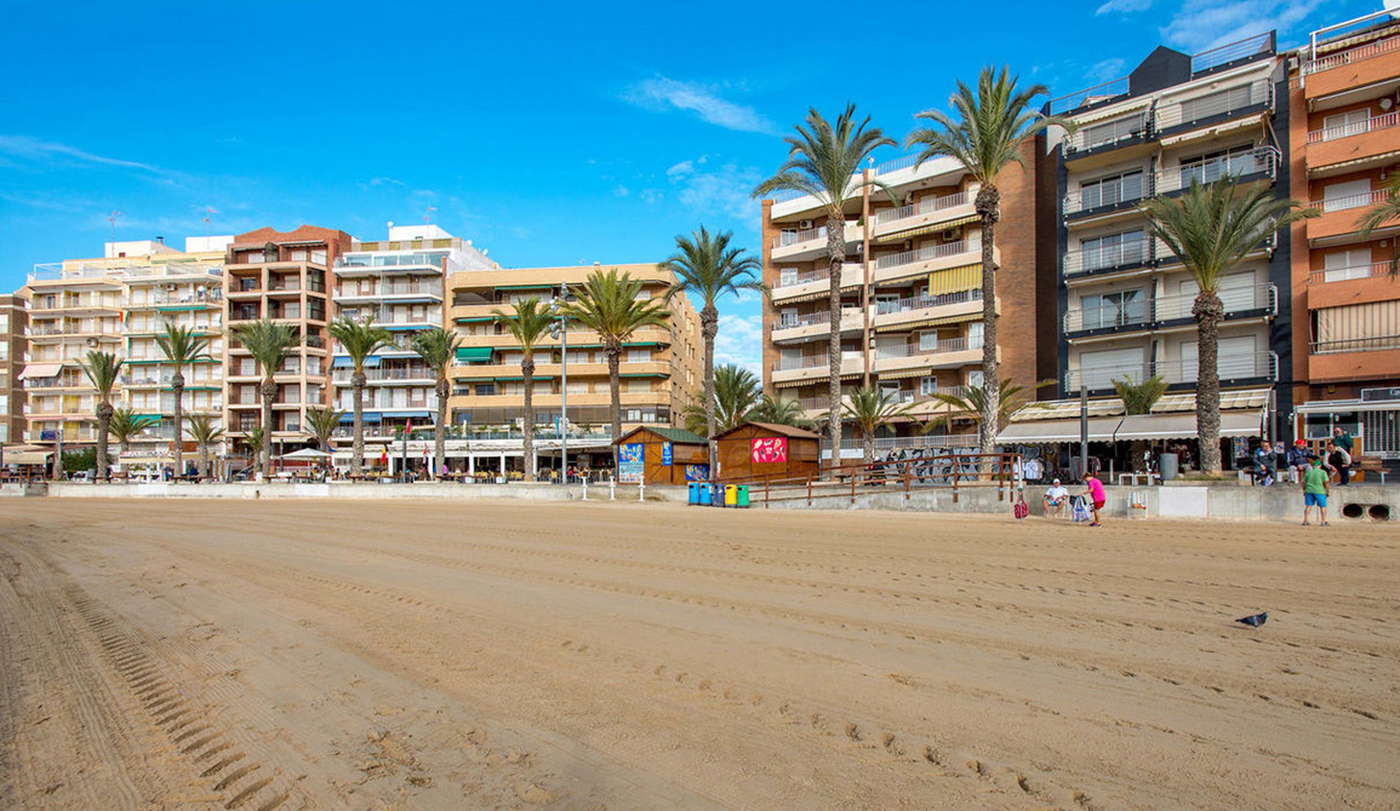 Un hotel frente a la playa con varios pisos, palmeras y una playa de arena.