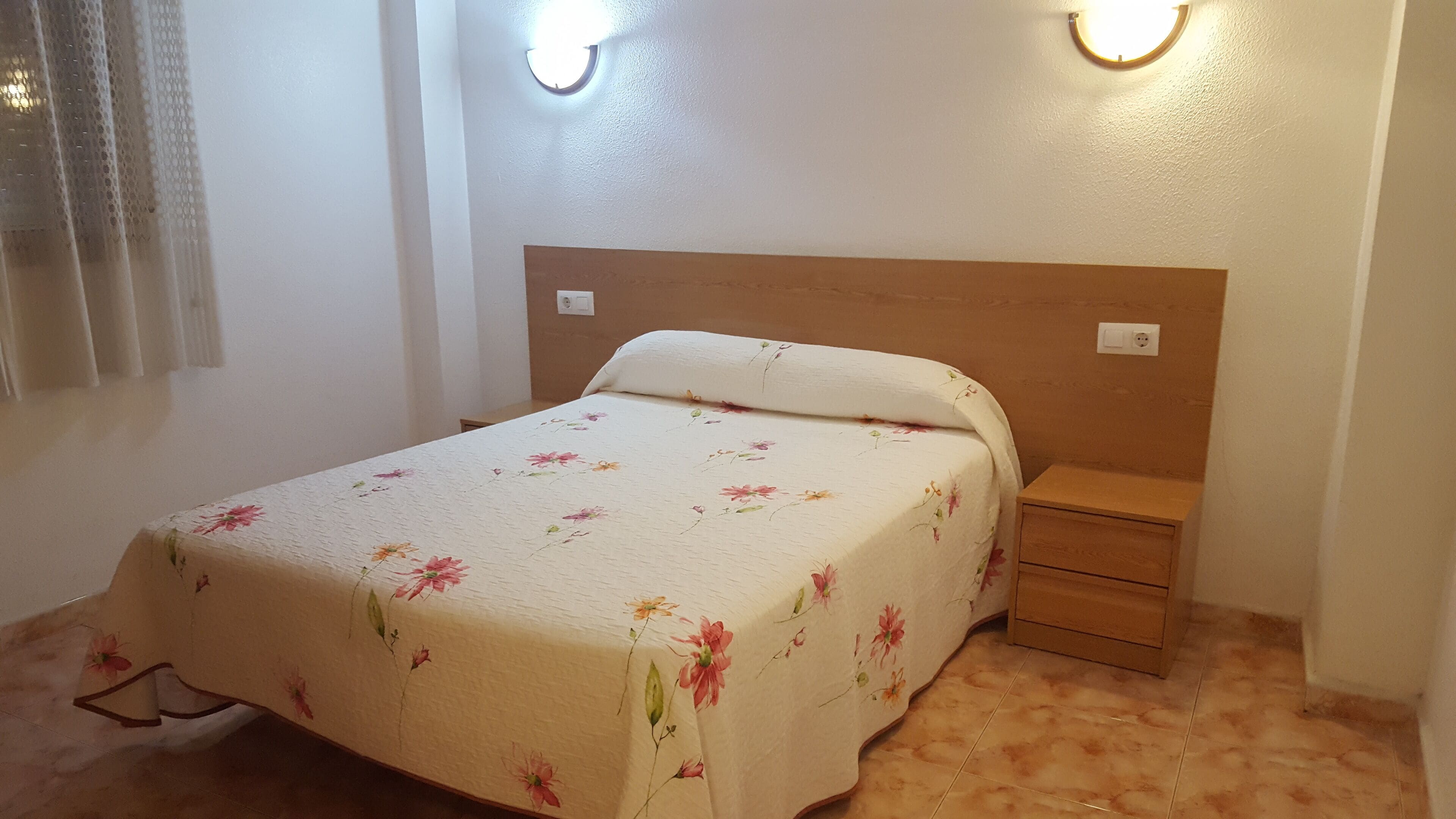 A bedroom with a bed, a nightstand, and two wall-mounted lights.