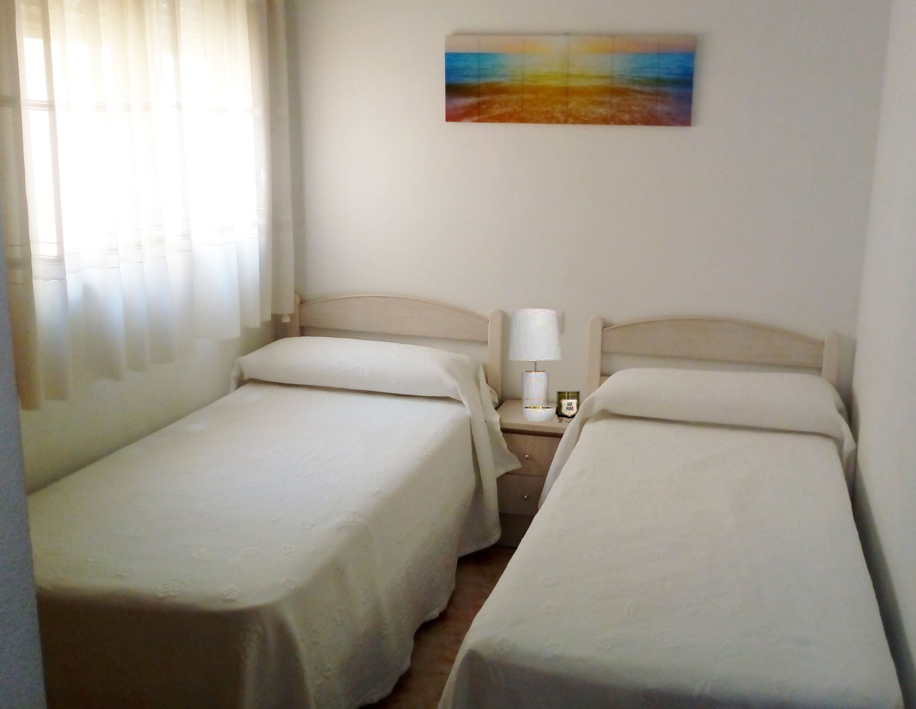 Una habitación de hotel con dos camas individuales, una mesita de noche con lámpara y un cuadro en la pared.