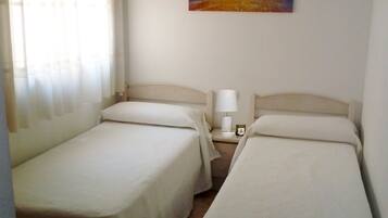 A hotel room with two single beds, a nightstand with a lamp, and a painting on the wall.